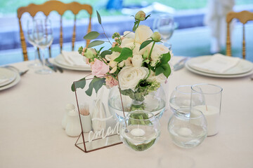 Beautiful floral arrangement of rose flowers and greenery on wedding table in restaurant, copy space. Luxury wedding decorations. Table setting