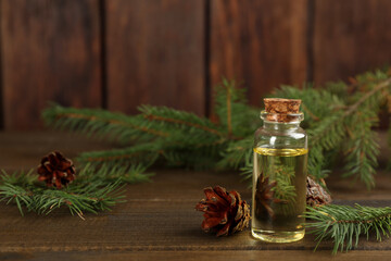 Pine essential oil, cones and branches on wooden table. Space for text