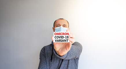 COVID-19 omicron variant symbol. White card, words Omicron covid-19 variant. A young man in a grey...