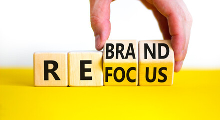 Refocus and rebrand symbol. Businessman turns cubes and changes the word 'refocus' to 'rebrand'. Beautiful yellow table, white background. Business, refocus and rebrand concept. Copy space.