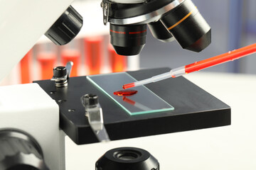 Dripping sample of red liquid onto slide under microscope in laboratory, closeup