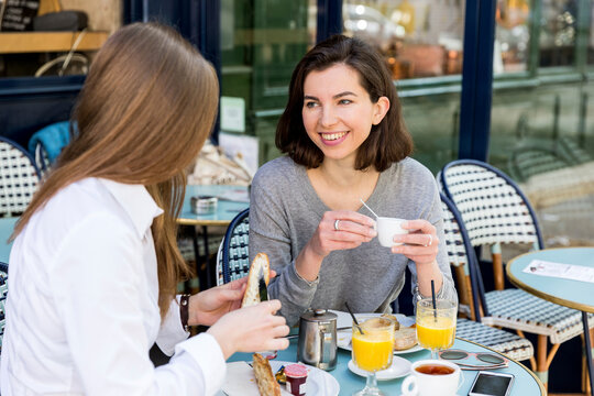 Young woman talking with friend and buttering baguette at cafe