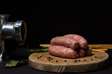 Raw meat sausages on a wooden board on a black background. Homemade sausages in a natural casing next to a steel meat grinder. Meat products. Home cooking