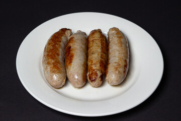 Fried meat sausages on a plate on a black background. Homemade sausages in a natural casing. Meat products. Home cooking