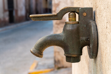 close-up to an old metal tap, on the wall of a street fountain.