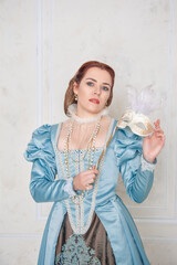 Beautiful young woman in medieval style dress with mask in the room