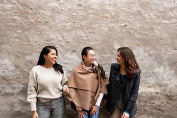 Obraz na płótnie Canvas Three friends laughing. Females multiracial group having fun. Old city wall on background with copy space.