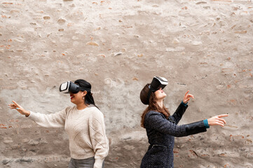 Two Young women enjoy virtual reality glasses. Old city wall with copy space on background.