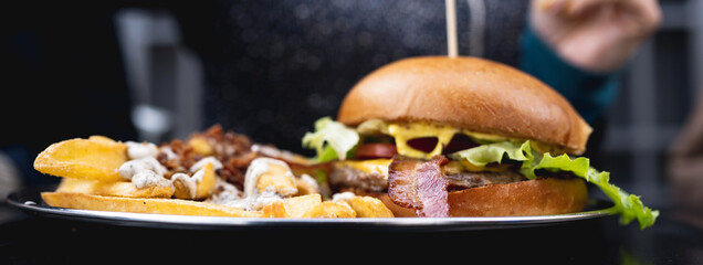 Horizontal banner or header Close-up combo menu with gourmet hamburger and french fries with sauce on table. Unrecognizable woman on background