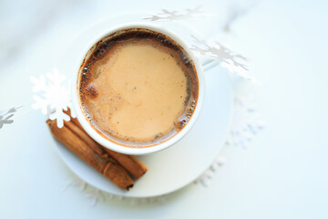 A cup of coffee over Christmas bokeh garlands in the house on the table with a sweater in the background and decorations. Winter mood, festive decoration, magical Christmas.