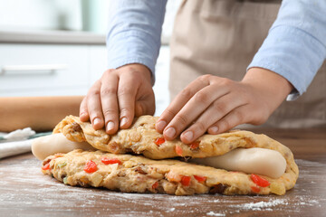 Woman putting marzipan into raw dough for Stollen at wooden table, closeup. Baking traditional German Christmas bread