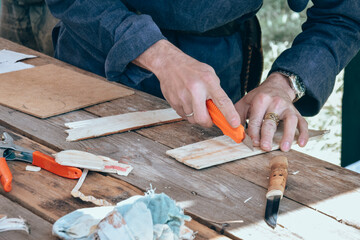 A man cuts with a knife on a wooden table. The craftsman makes wooden products.
