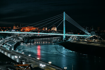 Fototapeta na wymiar Night city. City lights. Urban architecture. Illuminated bridge over the river.