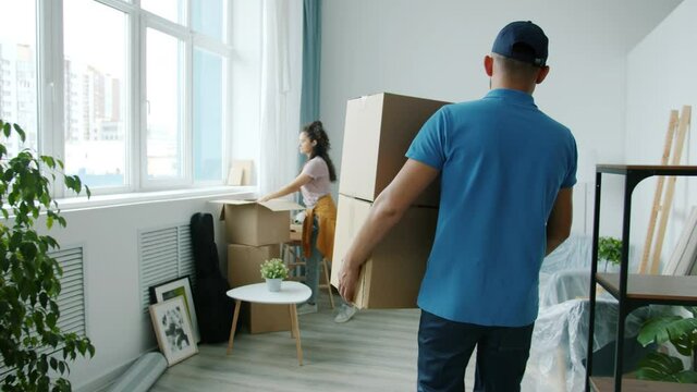 Slow motion of worker in uniform bringing cardboard boxes and talking to homeowner indoors in light studio. Relocation service and people concept.