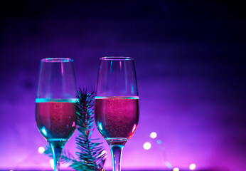 Two glasses of sparkling wine or champagne, neon Christmas background. Christmas Tree branch, copy space