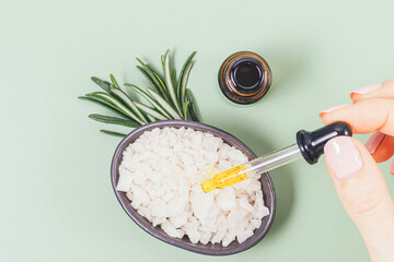 Female hand adding drop of essential oil with pipette to bowl of sea salt