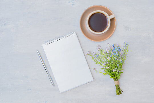 Flat lay composition with a mockup notebook, a cup of coffee and small blue flowers on a light background
