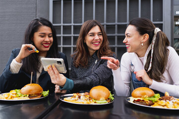 Group of females friends sitting at restaurant table eating burgers and laughing each other. Togetherness concept.