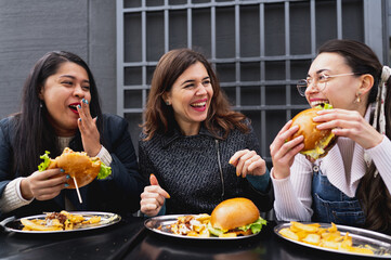 Group of multiracial young attractive women sitting at table having fun and laughing while eating burgers.