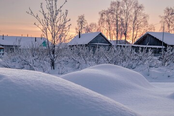 Beautiful winter view of the outskirts of the village at sunset. Rocks covered with snow in the foreground