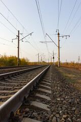 In the center there are parallel railway tracks and poles of electric wires extending into the distance at sunset