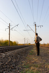A man walks along the center of the railroad tracks into the distance. Leaving road at sunset