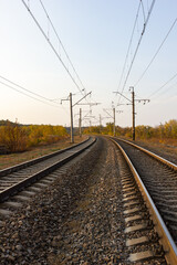 In the center there are parallel railway tracks and poles of electric wires extending into the distance at sunset