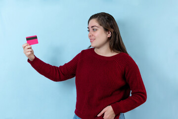 Young woman holding a credit card, isolated over light blue wall.