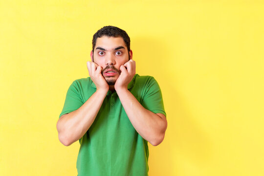 Scared young man. Portrait of nervous guy gestures in panic, isolated over yellow background.