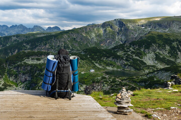 A man with a full backpack and bedding on his sides stands on top of a mountain enjoying the breathtaking stunning scenery. Mountain lake view