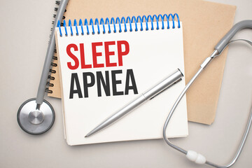 White notepad with the words sleep apnea and a stethoscope on a blue background. Medical concept