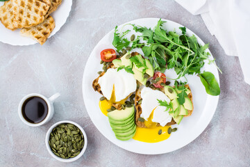 Healthy breakfast. Poached eggs on toast with avocado pieces, arugula, mizuna and chard leaves and cherry tomatoes on a plate on a served table. Flexetarian diet. Top view. Copy space