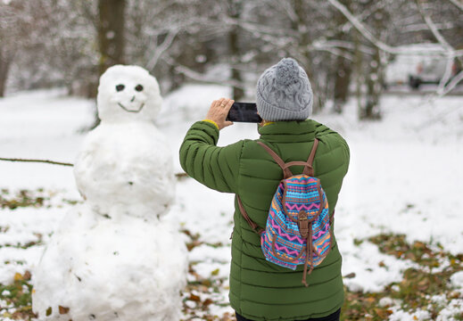 woman taking photo of snowman in forest in winter season -