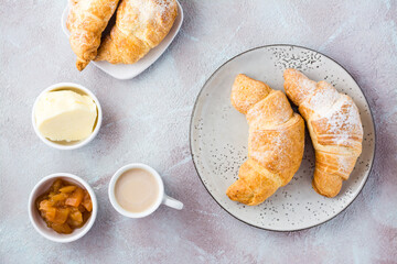 Fresh crispy croissants on plates, a cup of coffee and bowls with jam and butter on a light textured background. Coffee break or breakfast. Top view