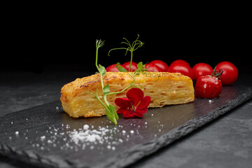 Dauphinua potato gratin with cherry tomatoes on a black stone