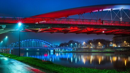 Kładka Bernatka i Most Piłsudskiego po zmroku podświetlone na czerwono i niebiesko