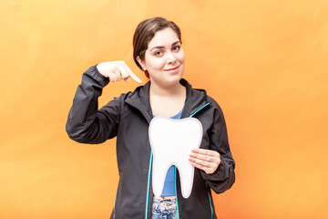 Girl pointing to a tooth shape, isolated over orange background.
