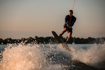 athletic male wakeboarder jumps with wakeboard over splashing river. Summertime watersports activity