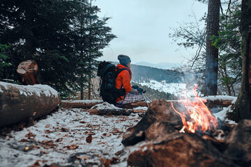 Rest in the snowy mountains by the fire. Beautiful hiker girl enjoys mountain scenery.