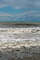 stormy waves of the Mediterranean sea run over the rocky summer beach against the backdrop of a blue cloudy sky