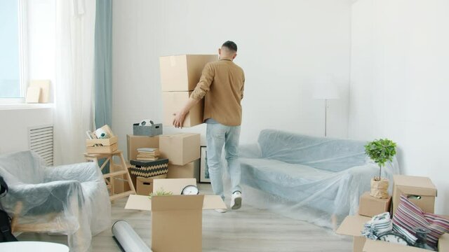 Slow motion of Arab guy mover carrying cardboard boxes in modern apartment walking with packages alone. Accommodation and delivery service concept.