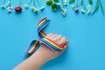 Rainbow ribbon in child hand. Blue mint paper background with wild flowers. Thank you NHS workers, doctors and nurses Flat lay, top view, minimal composition. Creative concept background.