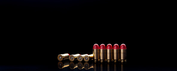 Pistol cartridges with red silicone coating. Bullets for a pistol on a dark back. Reflections on a black surface.