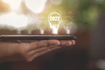 business in 2022,A light bulb that is placed on a smartphone Business man's hand Bright in the year...