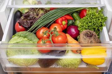 Vegetable compartment of the refrigerator full of fresh vegetables. Open fridge, drawer filled with...