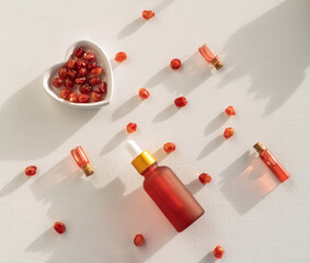Red dropper bottles of pomegranate serum or oil for face and body lying on a white table