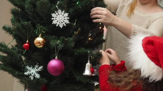 Family decorating a Christmas tree with boubles in the living room. mom and daughter decorate the tree with different toys home, family holidays, happy new year and christmas