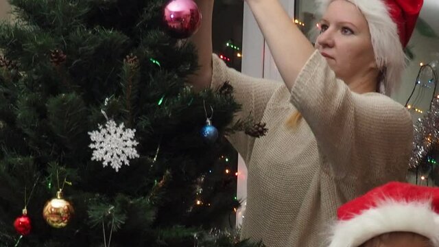 Family decorating a Christmas tree with boubles in the living room. mom and daughter decorate the tree with different toys home, family holidays, happy new year and christmas