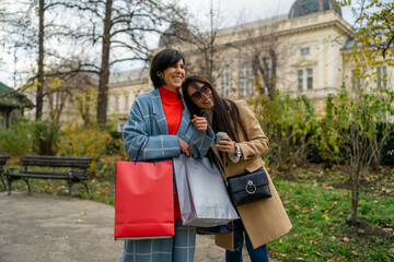 Fototapeta premium Two beautiful young women with shopping bags walking down the street