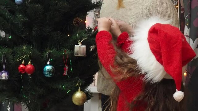 Family decorating a Christmas tree with boubles in the living room. mom and daughter decorate the tree with different toys home, family holidays, happy new year and christmas
